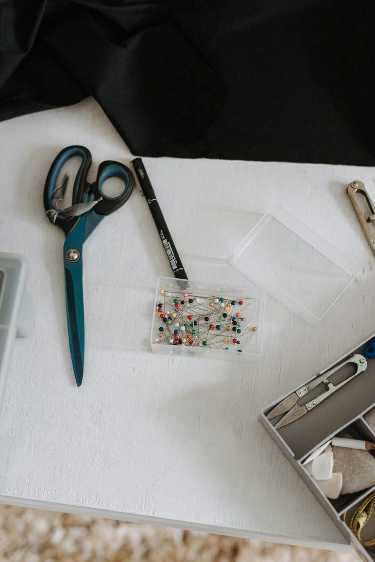 Top view of small plastic box with pins and scissors placed on table with sewing supplies in modern light workshop